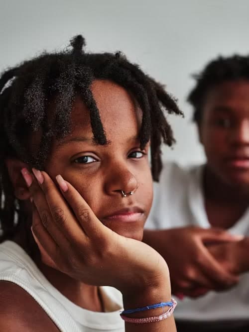 A young person resting their cheek on one hand, with another person seated behind them.