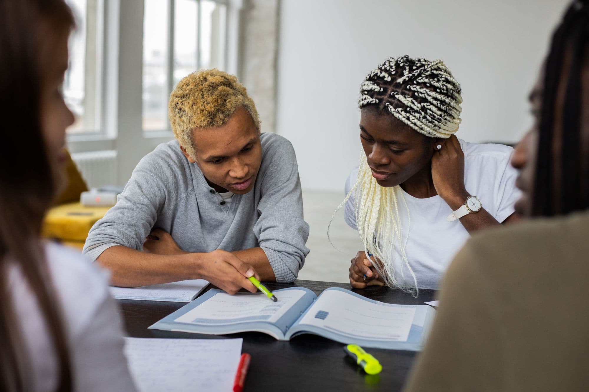 Adults gathered around a table, reading a textbook together.