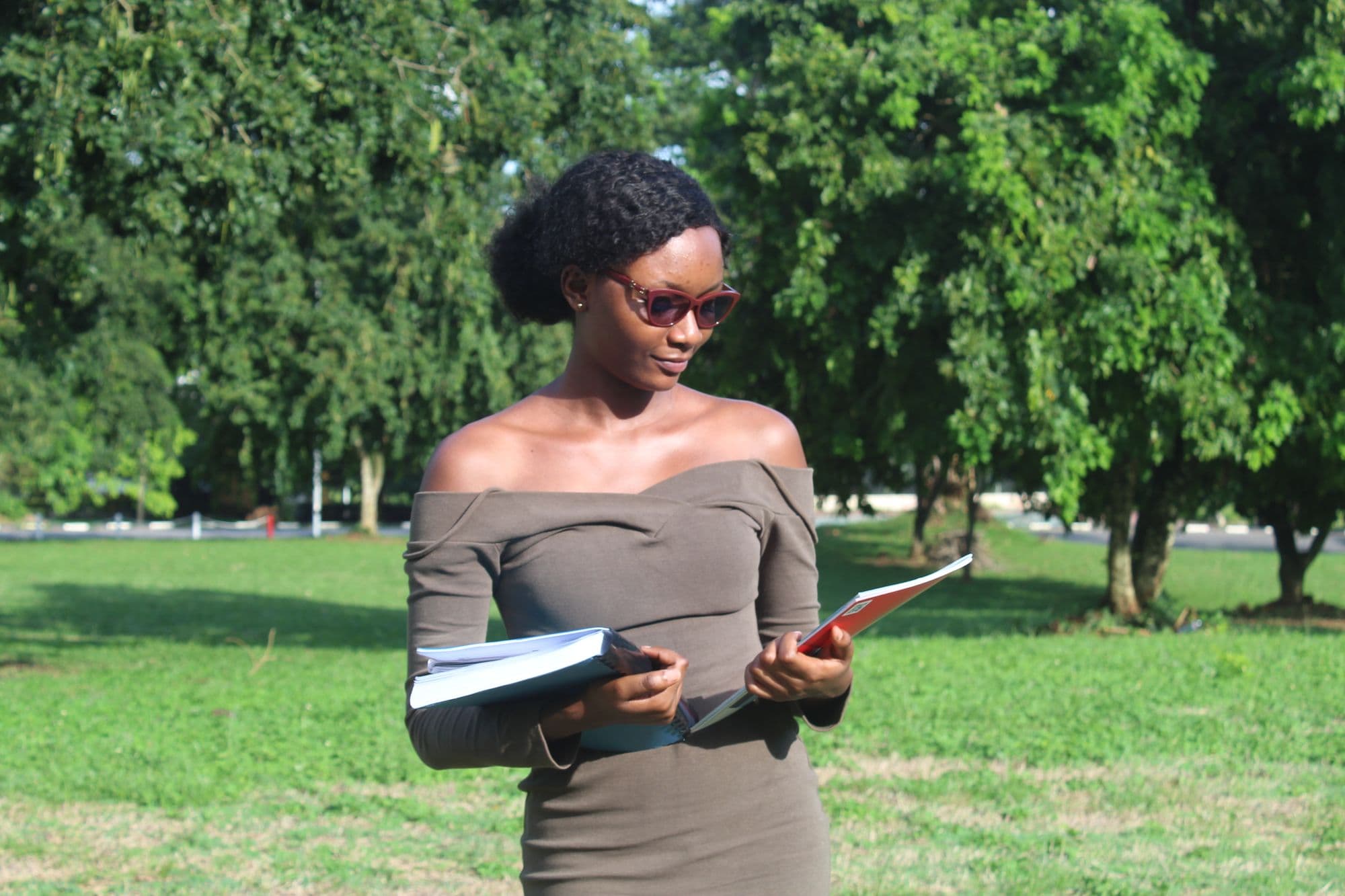 A woman standing in a park in Kumasi, reading papers she is holding.