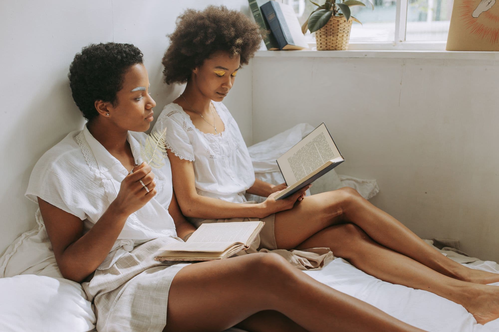 Two women sitting together by a window, reading books.