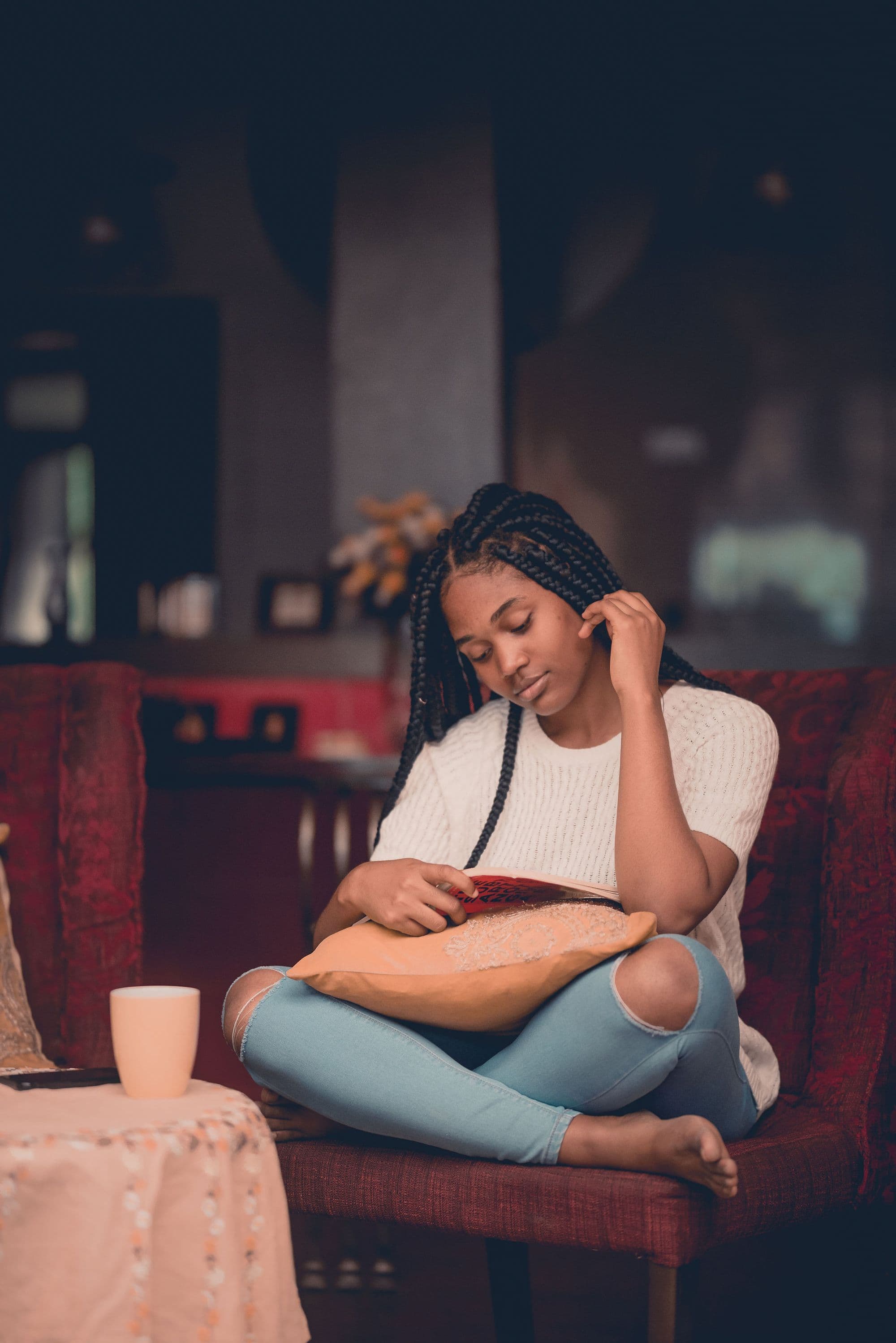 A young woman sitting on a sofa at home, reading a book.